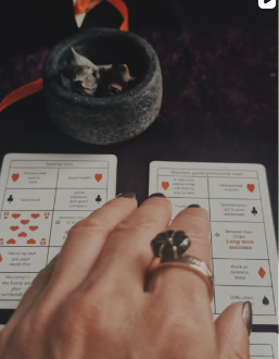 A reader's hand resting on playing cards beside a smoking cauldron